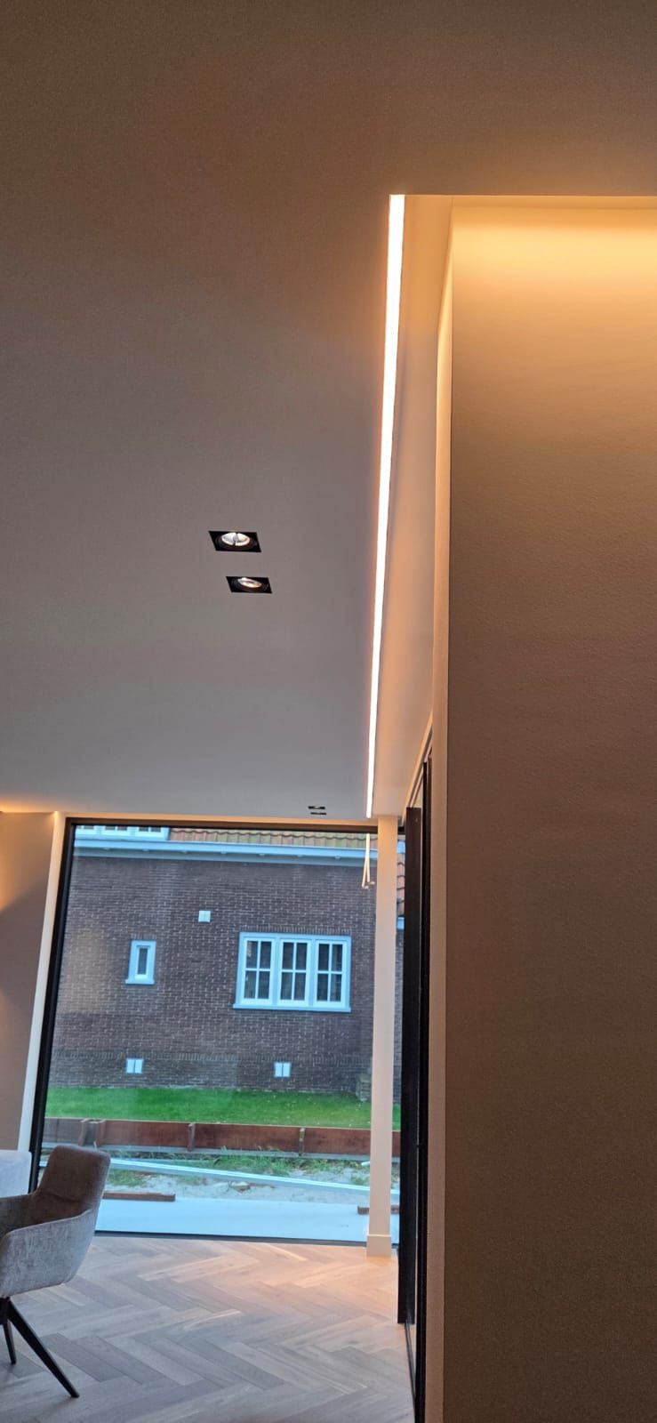 Afgewerkte koofverlichting, LED-lijn en zwarte inbouwspots in een modern interieur met uitzicht op een Nederlandse woning