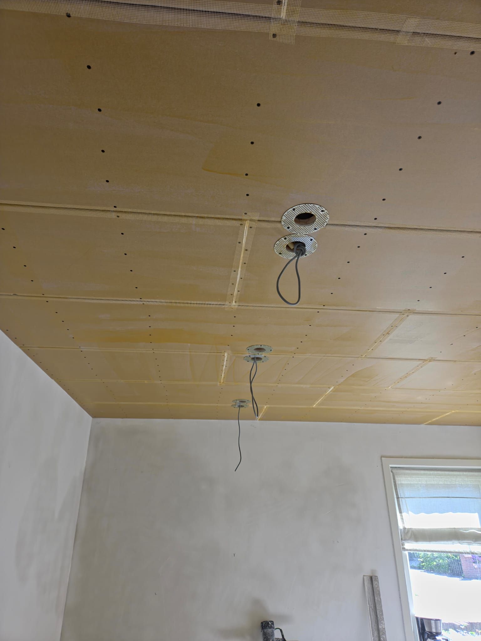 Werk in uitvoering: plafond met uitsparingen, beugels en hangende kabels voor inbouwspots tijdens renovatie